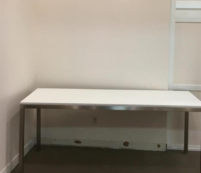 Carpet and baseboard removed under a white table with silver front