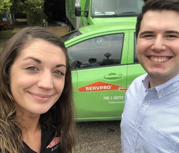 A man and woman standing in the street in front of SERVPRO cars at a home