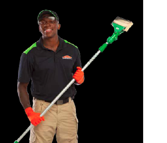SERVPRO technician with black shirt and khakis holding a pole with a soot sponge attached