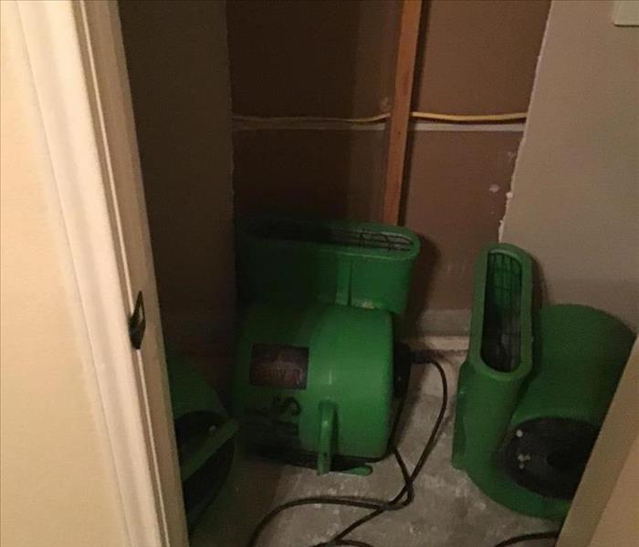 Three SERVPRO green industrial air movers pointed at an exposed wall cavity in a closet