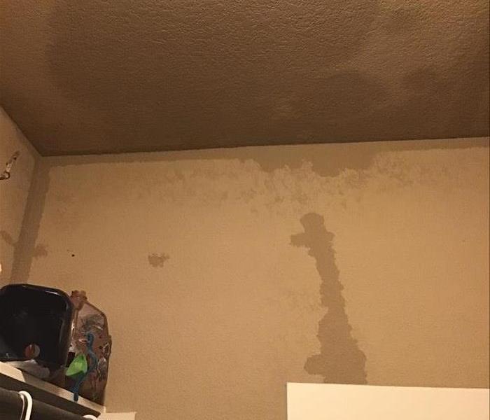 a beige ceiling and wall in a closet with a large wet spot and water along where the ceiling and wall meets