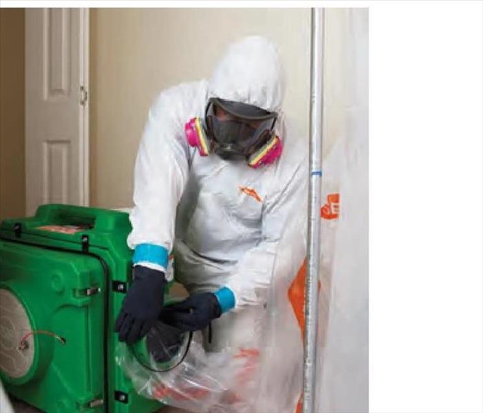 SERVPRO Technician in white PPE suit with respirator in front of a green air scrubber