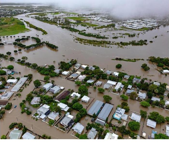 An aerial view of a flooded neighborhood with submerged houses, roads, and surrounding landscapes under water.