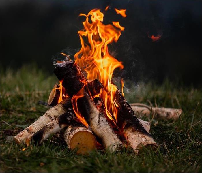 campfire-style fire pit with flames emerging from the top of the logs on the dark green grass