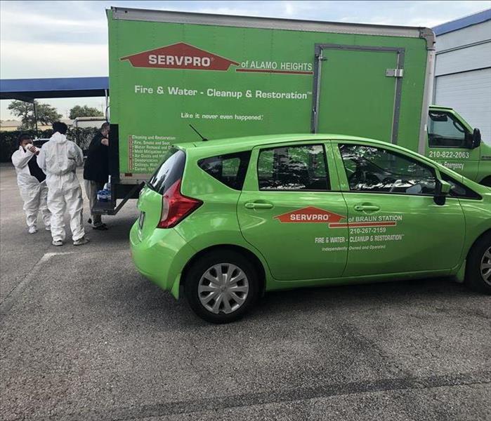 3 people donning PPE in front of a large green box truck and a SERVPRO® green hatchback